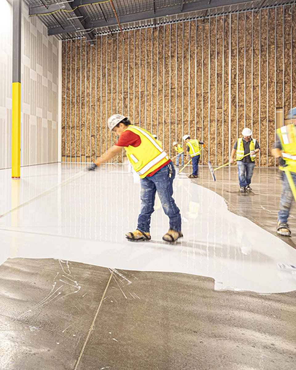 A crew pulling a coating across bare concrete, wet edge visible.